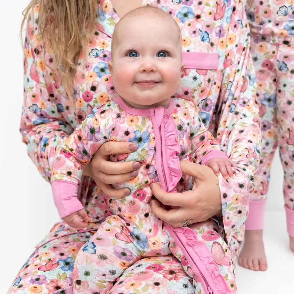Baby in a matching floral and butterfly print zip-front romper with pink trim