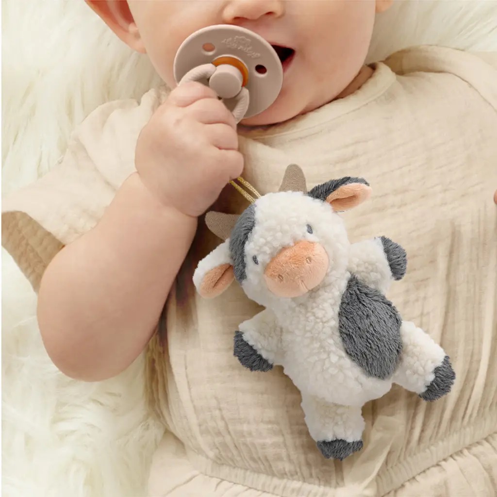 Baby holding Itzy Ritzy plush cow pacifier pal