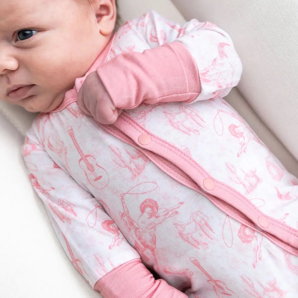 Newborn in a white and pink snap-front onesie with cowgirl and guitar print and pink cuffs