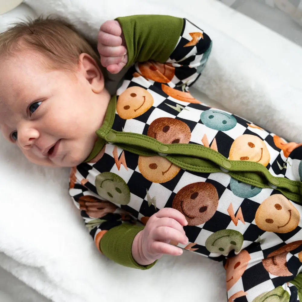 Smiling baby in a black and white checkered snap-front onesie with colorful smiley faces and olive green cuffs