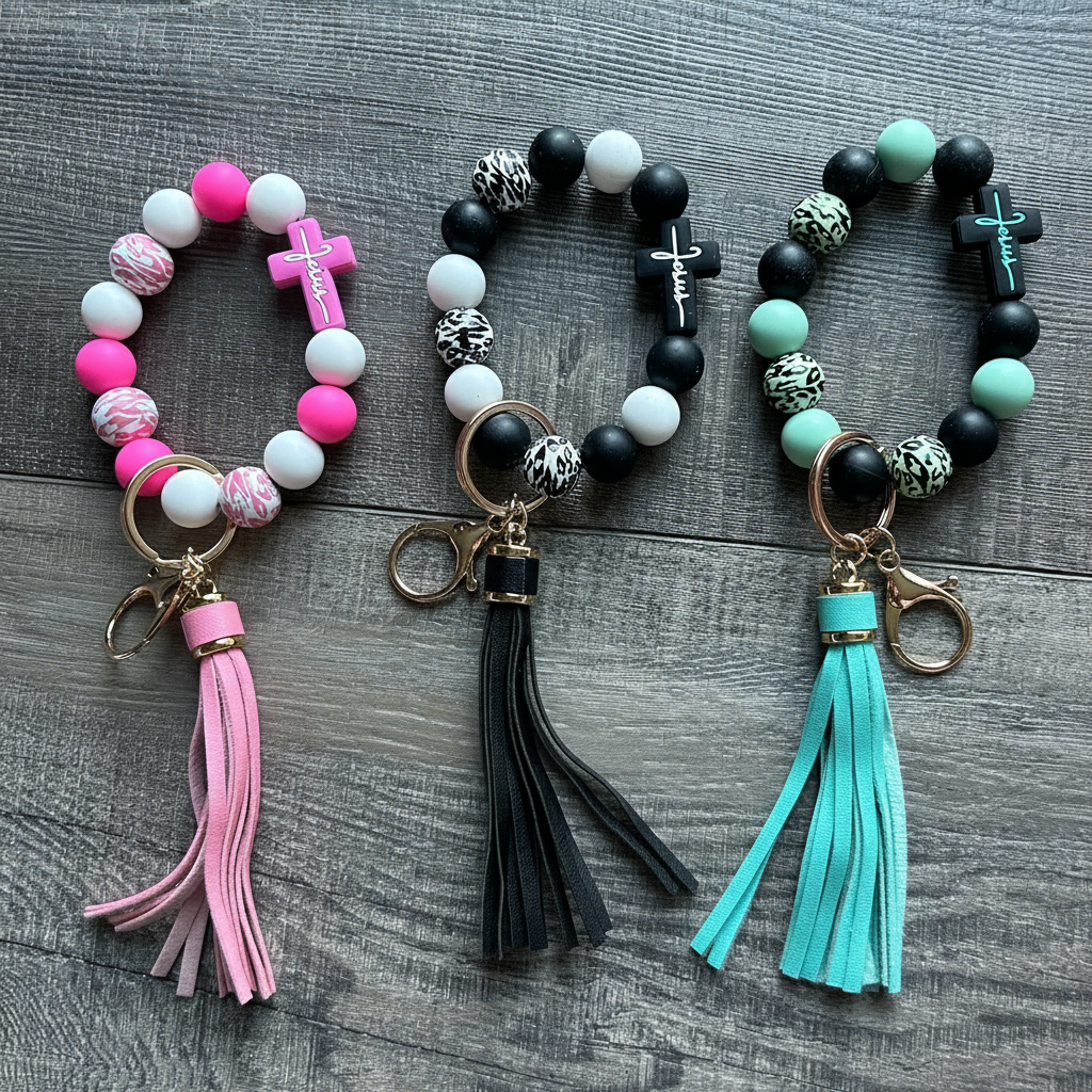Three faith-inspired silicone bead wristlet keychains with cross charms in pink, black leopard, and mint with tassels